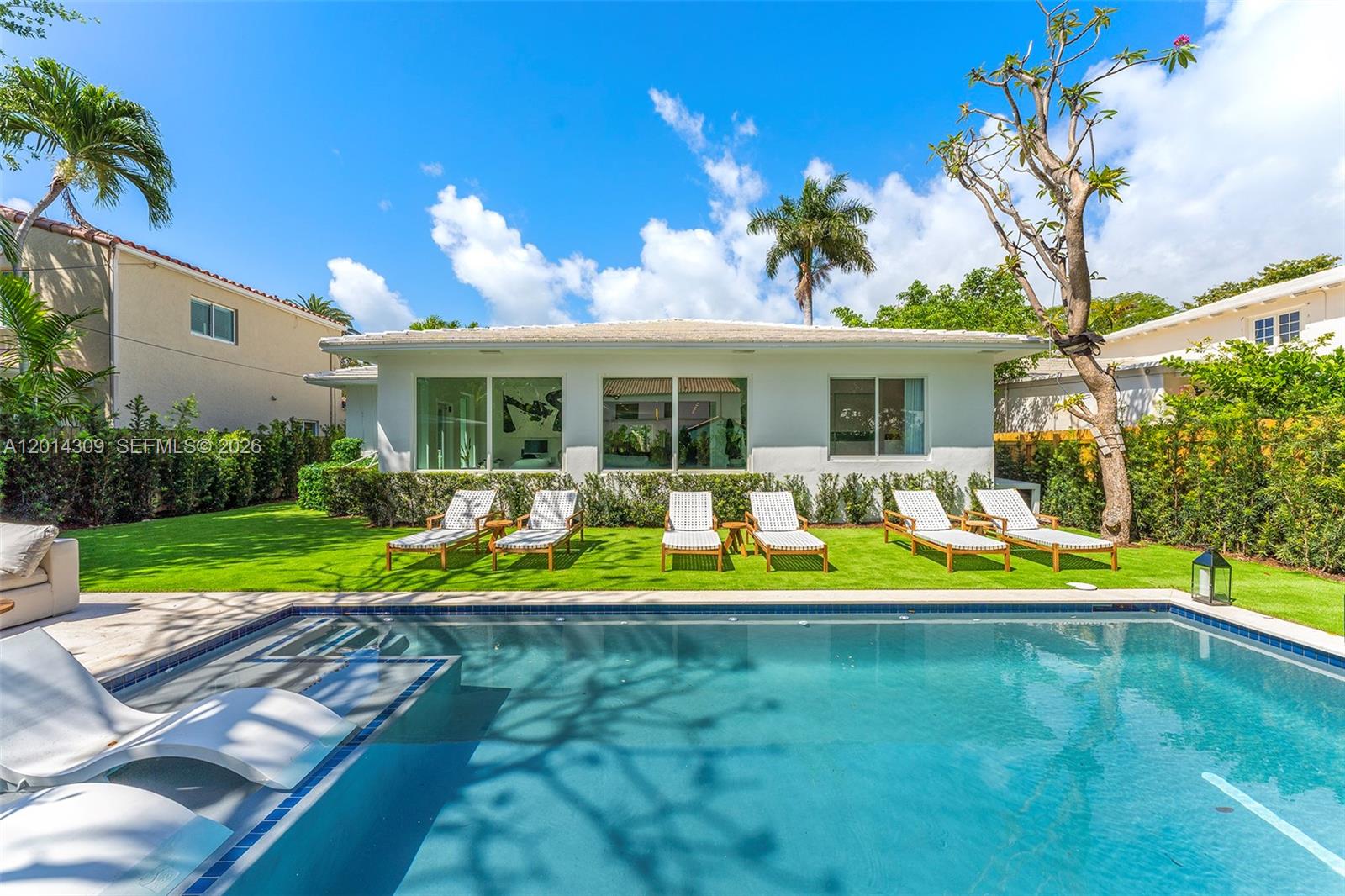 A swimming pool sits in front of a white house with six lounge chairs on grass — 6145 La Gorce Dr, Miami Beach FL 33140, MIAMI BEACH, FL