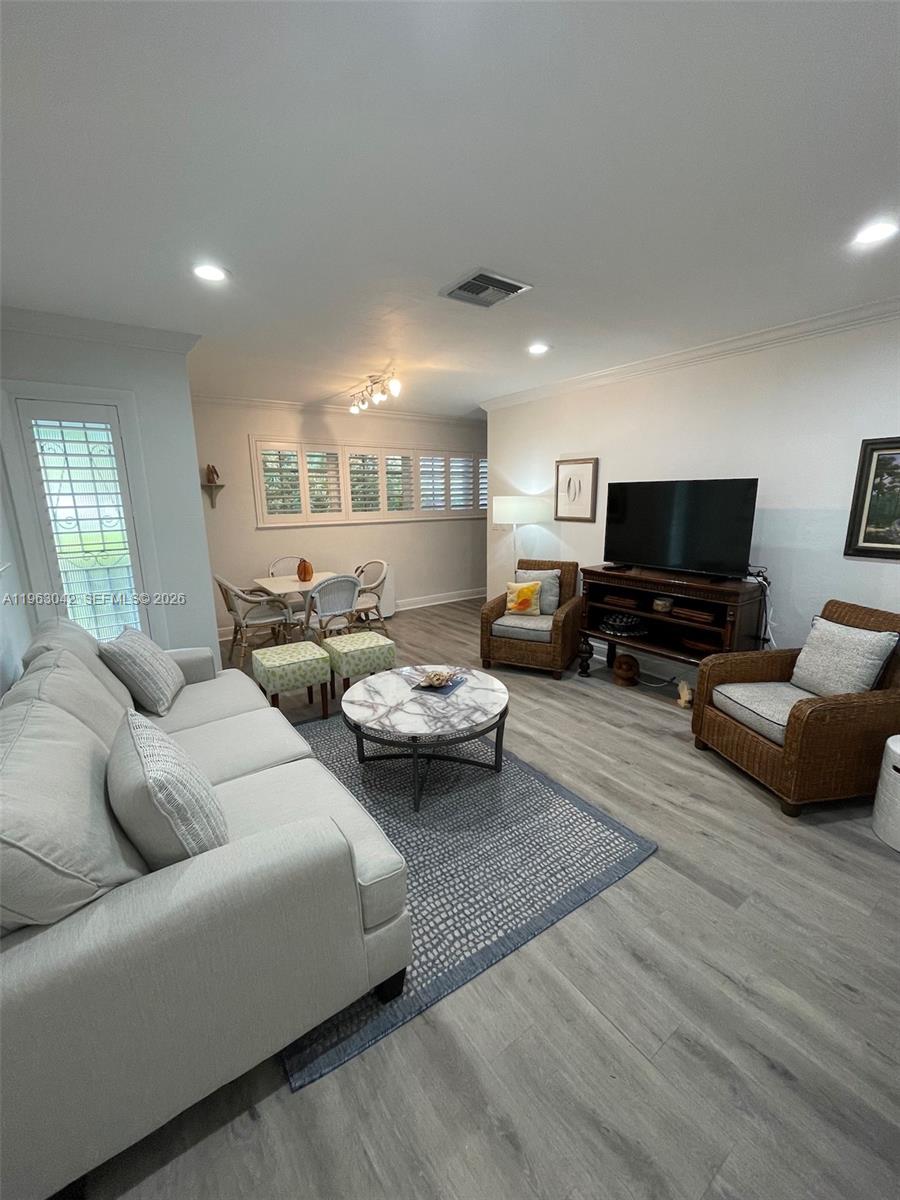 A living room features a grey sofa, wicker armchairs, a marble coffee table, and flooring — CORAL GABLES, FL