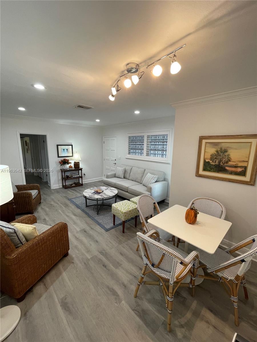 This open-concept living and dining area features light wood-look flooring and a track lighting fixture — CORAL GABLES, FL