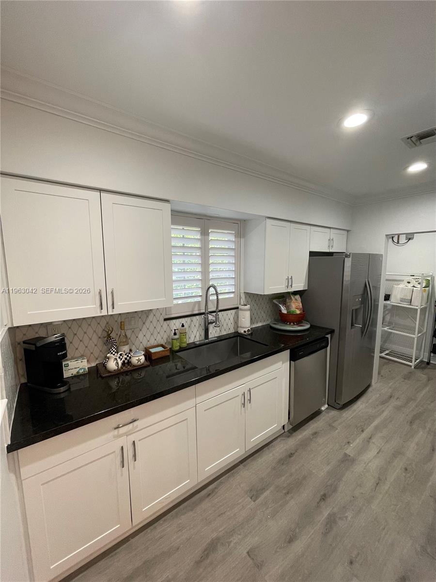 A kitchen features white cabinets, black countertops, stainless steel appliances, and light wood-look flooring — CORAL GABLES, FL