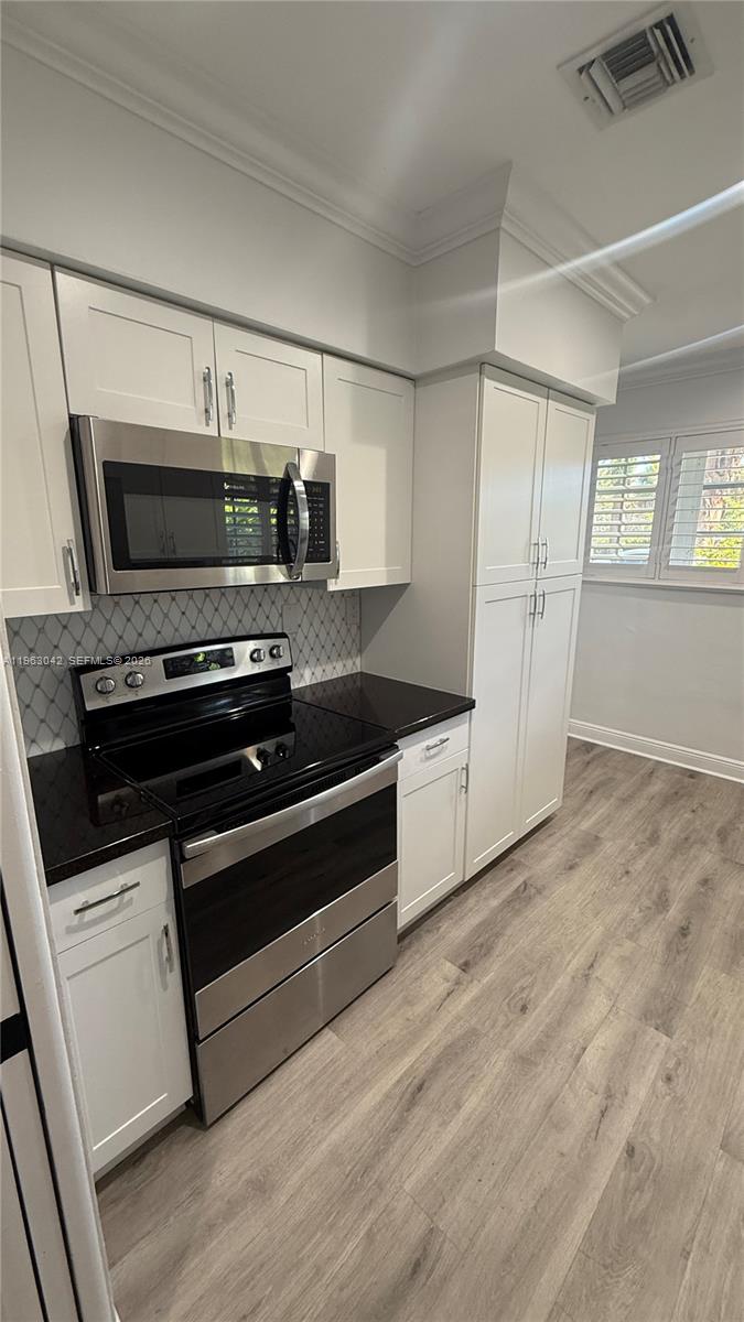 A kitchen features white cabinets, stainless steel appliances, black countertops, and light wood-look flooring — CORAL GABLES, FL