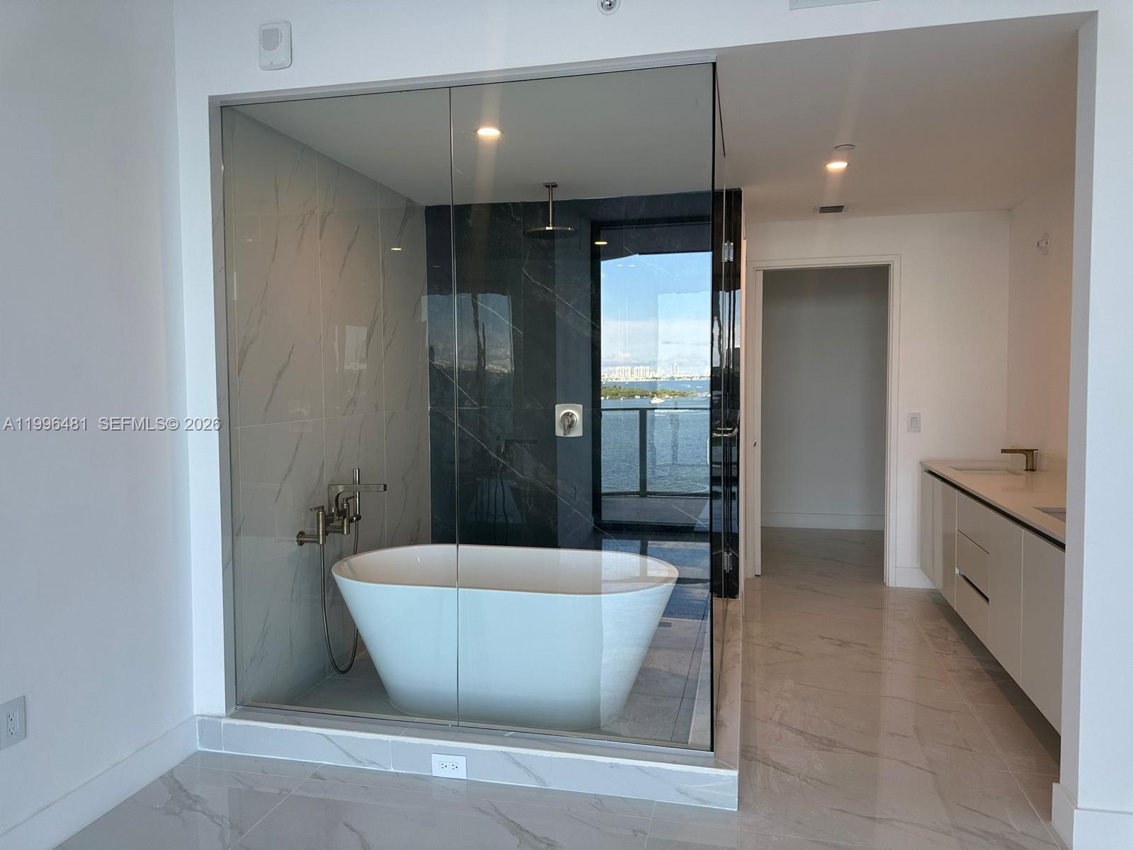 A modern bathroom features a glass-enclosed soaking tub and shower with marble-style tile flooring — 700 NE 24th # 504, Miami FL 33137, MIAMI, FL