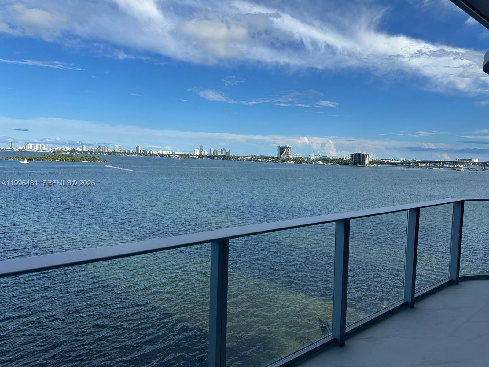 A balcony with a glass railing overlooks a wide bay and a distant city skyline — 700 NE 24th # 504, Miami FL 33137, MIAMI, FL
