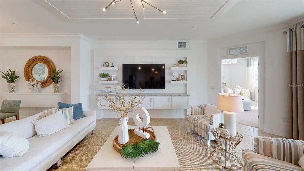 A bright living room features a white built-in media center, a sofa, and striped armchairs — 12913 SANTA MONICA COURT UNIT 74-102, VENICE, FL
