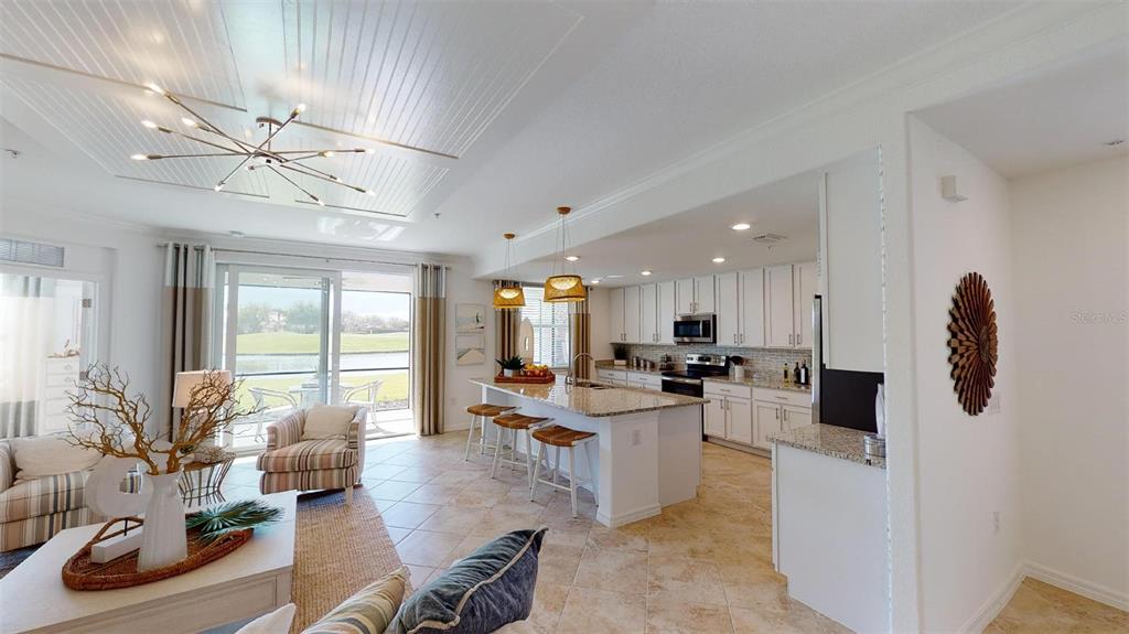 An open-concept kitchen and living area features white cabinetry, a granite island, and tile floors — 12913 SANTA MONICA COURT UNIT 74-102, VENICE, FL