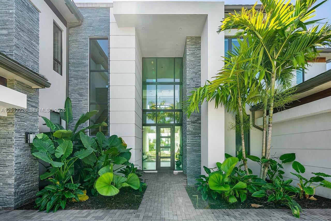 The exterior of a modern home features a stone-accented entryway with large glass windows — 17187 Brulee Breeze Way, Boca Raton FL 33496, BOCA RATON, FL