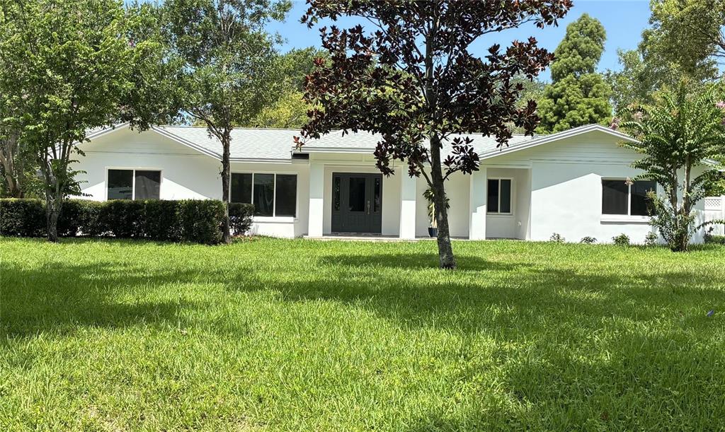 A white, single-story house with a dark front door sits behind a large green lawn — 1646 ROBIN HOOD LANE, CLEARWATER, FL