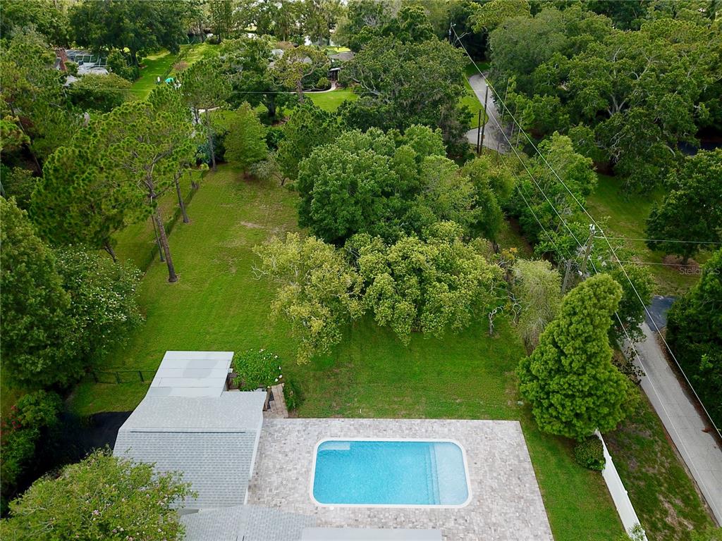 An aerial view shows a rectangular swimming pool with a stone patio and a large backyard — 1646 ROBIN HOOD LANE, CLEARWATER, FL