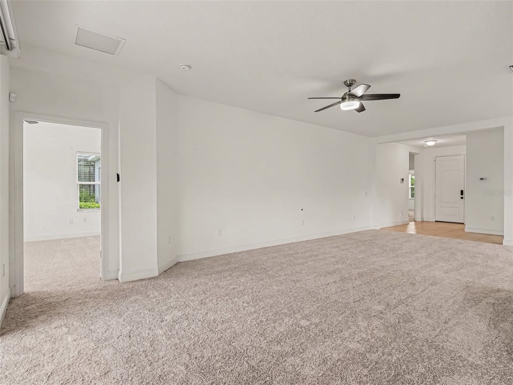 A carpeted living room features a ceiling fan and an entryway leading to a tiled foyer — 7521 RIDGELAKE CIRCLE, BRADENTON, FL