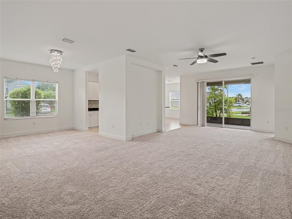 A spacious, carpeted living area features a crystal chandelier, ceiling fan, and sliding glass doors — 7521 RIDGELAKE CIRCLE, BRADENTON, FL