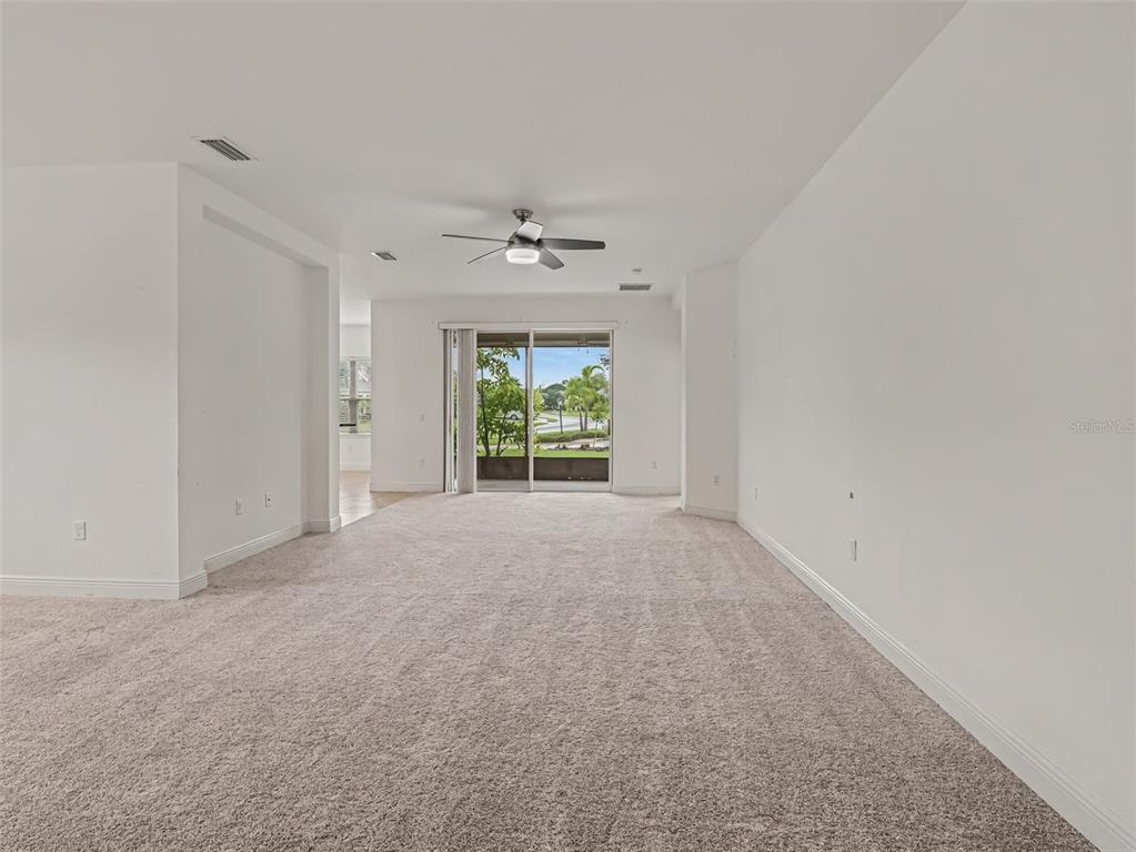 An empty living room features beige carpeting, white walls, a ceiling fan, and sliding glass doors — 7521 RIDGELAKE CIRCLE, BRADENTON, FL