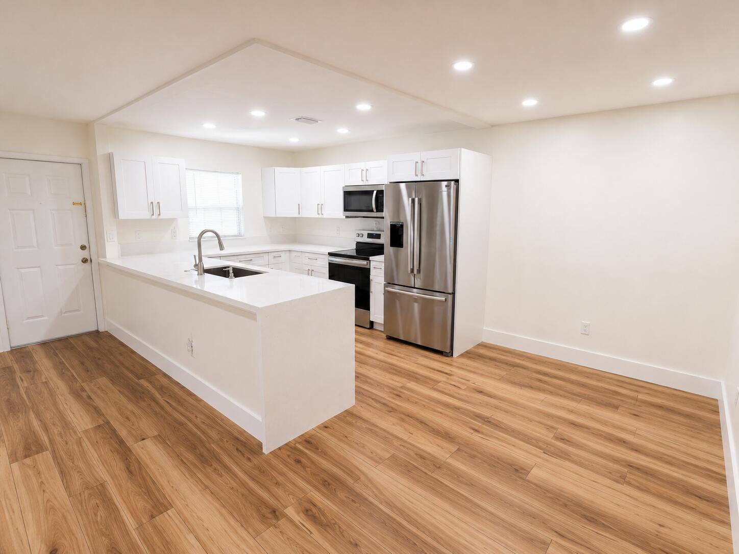 A modern kitchen features white cabinetry, stainless steel appliances, quartz countertops, and light wood flooring — 5424 Lakefront Boulevard # D, Delray Beach FL 33484, DELRAY BEACH, FL
