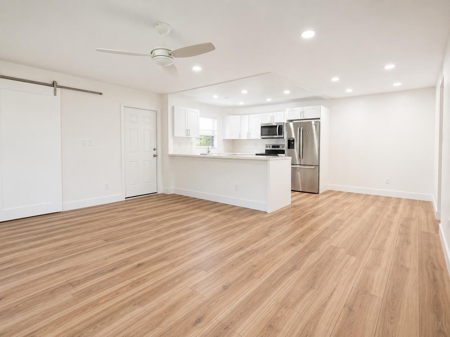 A bright, open-concept kitchen and living area featuring white cabinets, stainless appliances, and wood flooring — 5424 Lakefront Boulevard # D, Delray Beach FL 33484, DELRAY BEACH, FL
