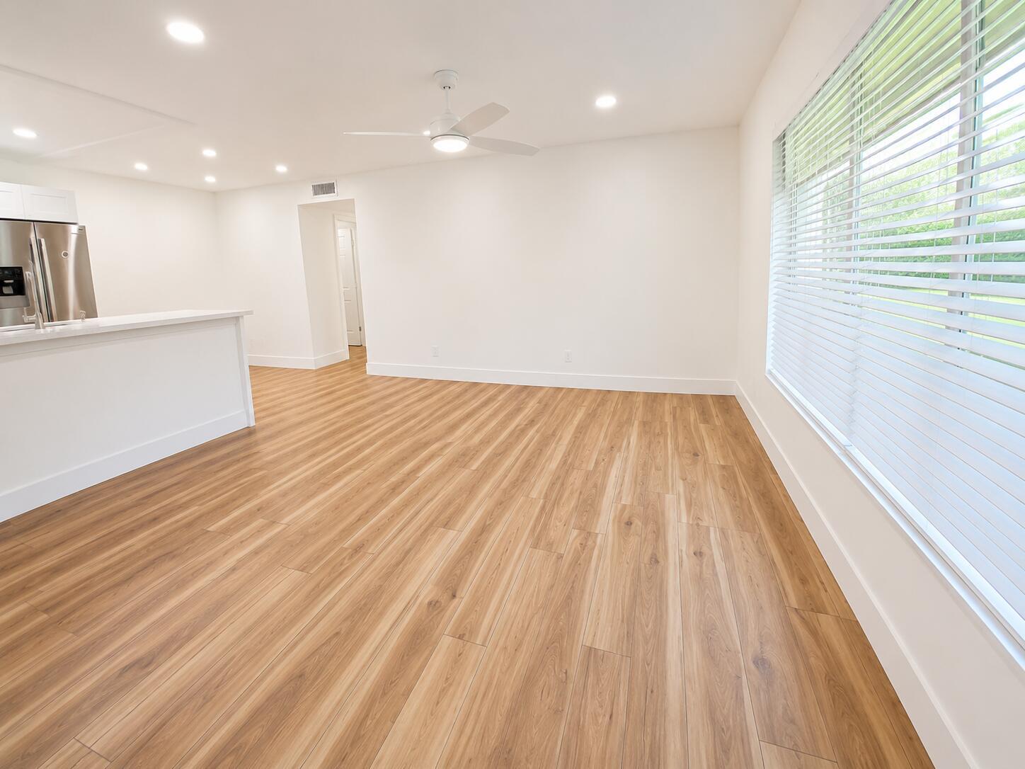 A bright, empty room features light wood-look flooring, white walls, a ceiling fan, and large windows — 5424 Lakefront Boulevard # D, Delray Beach FL 33484, DELRAY BEACH, FL