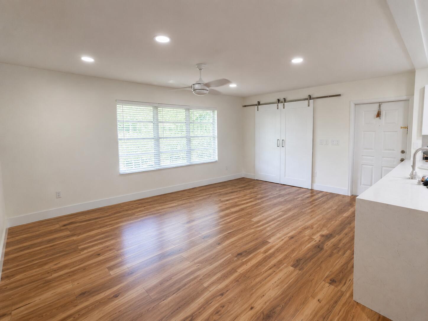 A bright, empty room features wood-look flooring, recessed lighting, a ceiling fan, and sliding barn doors — 5424 Lakefront Boulevard # D, Delray Beach FL 33484, DELRAY BEACH, FL