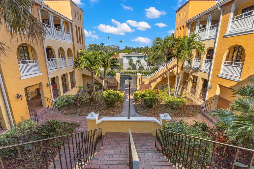 An elevated view of a courtyard between two yellow apartment buildings with brick staircases — 210 22ND AVENUE NE UNIT 15, ST PETERSBURG, FL