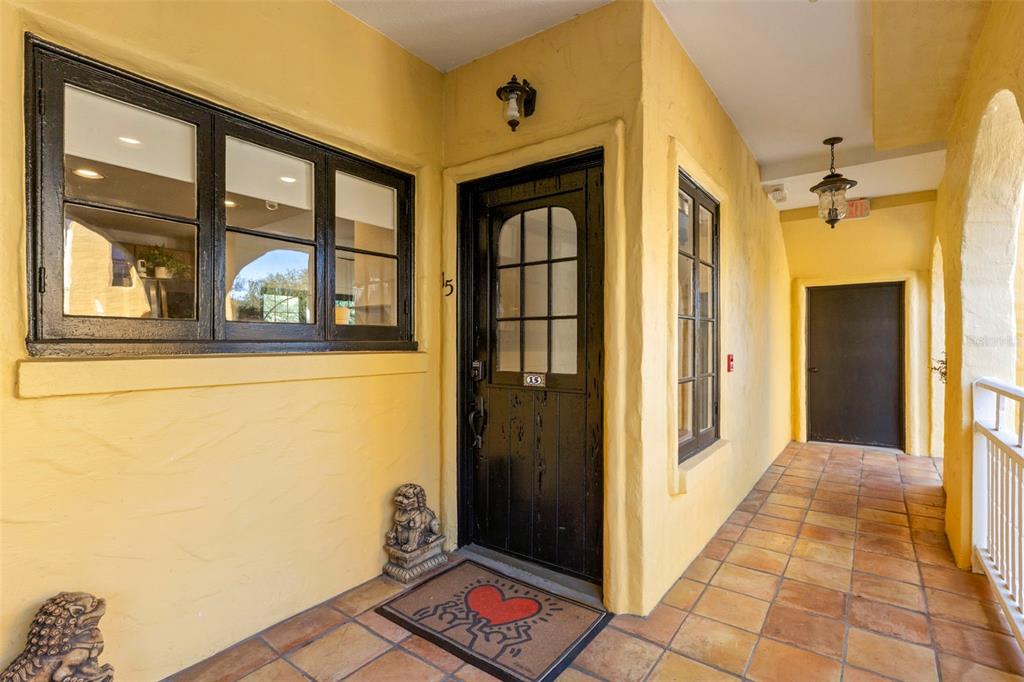 A yellow stucco exterior hallway features a black front door with a heart doormat — 210 22ND AVENUE NE UNIT 15, ST PETERSBURG, FL