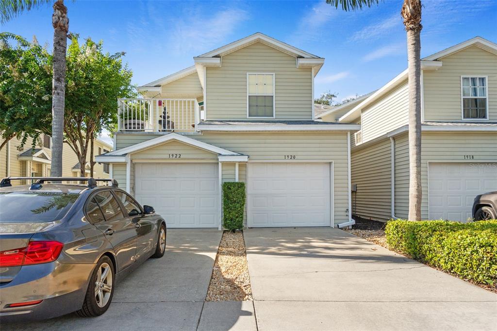 A two-story duplex with light green siding, two white garage doors, and a balcony — 1920 HAMMOCKS AVENUE UNIT 1002, LUTZ, FL
