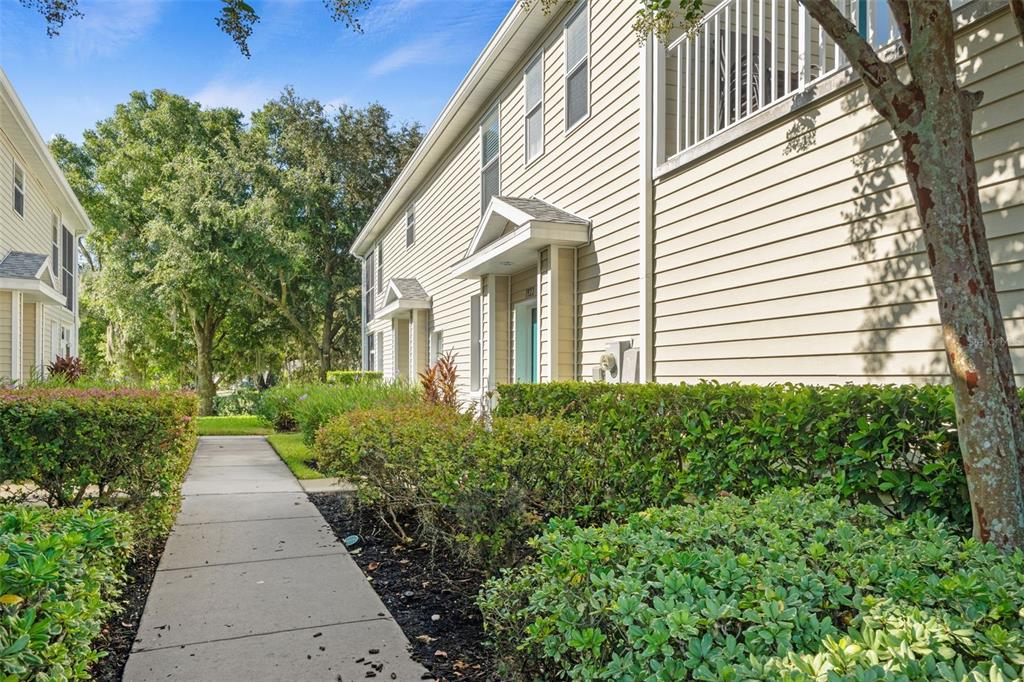 A sidewalk leads to the entrance of a two-story tan building with light-colored siding — 1920 HAMMOCKS AVENUE UNIT 1002, LUTZ, FL