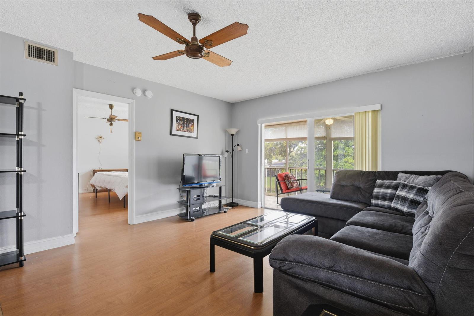 A living room features light gray walls, wood-look flooring, a sectional sofa, and a balcony — 7505 NW 5th Place # 203, Margate FL 33063, MARGATE, FL