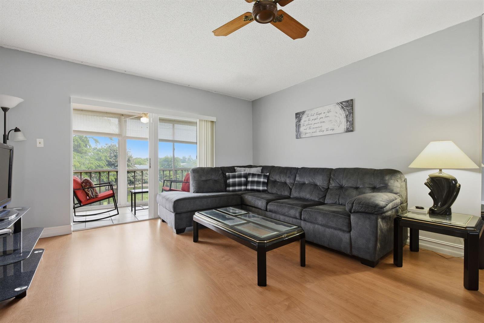 A living room features a grey sectional sofa, wood-look flooring, and a sliding glass door — 7505 NW 5th Place # 203, Margate FL 33063, MARGATE, FL