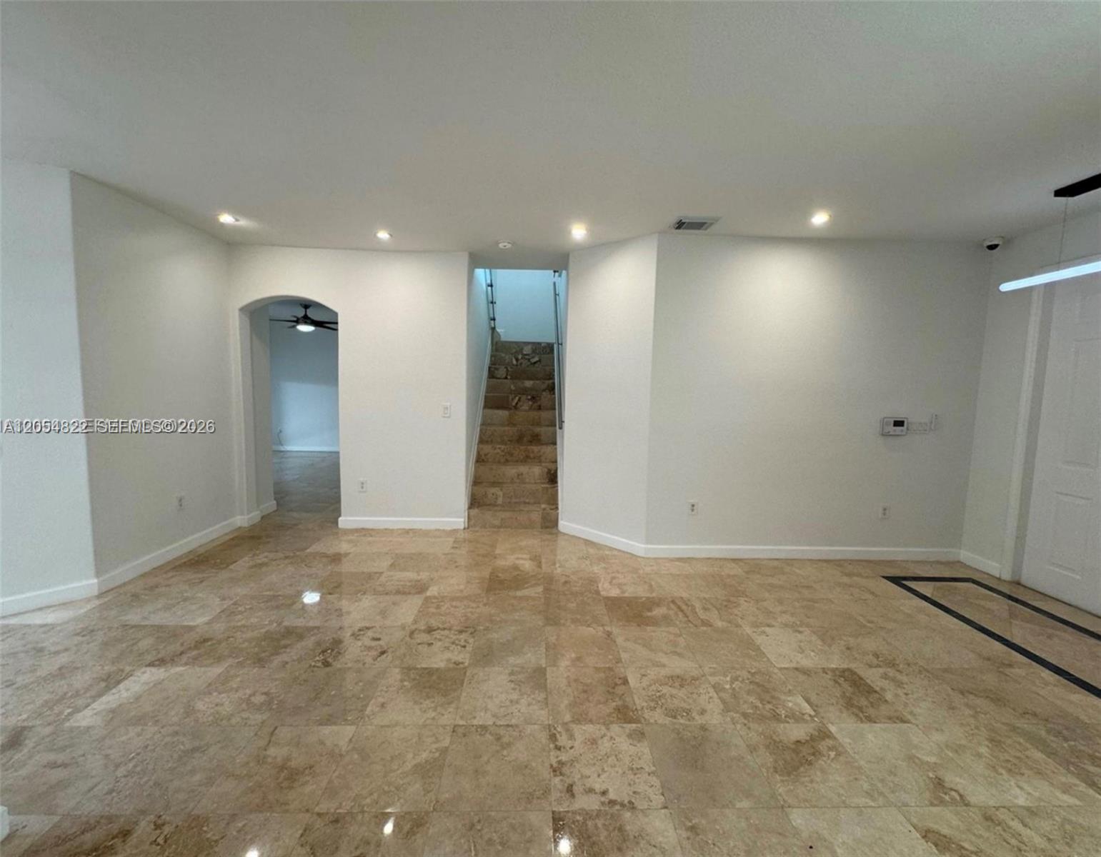A room with beige tile flooring features a central staircase and an arched doorway — 7563 NW 112th Pl, Doral FL 33178, DORAL, FL