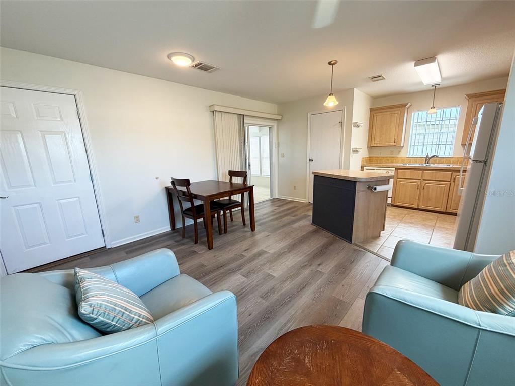 A living and dining area with light wood-look flooring, a kitchen island, and light blue chairs — 1503 23RD AVENUE W, BRADENTON, FL