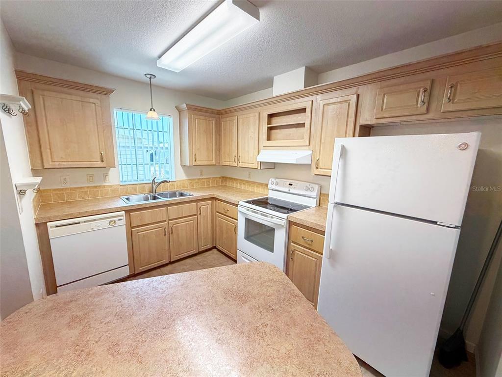 A kitchen features light wood cabinets, laminate countertops, white appliances, and a window with bars — 1503 23RD AVENUE W, BRADENTON, FL