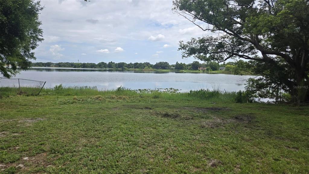 A grassy yard leads to a lake view framed by large trees under a cloudy sky — DOMINO COURT LOT 9, ORLANDO, FL