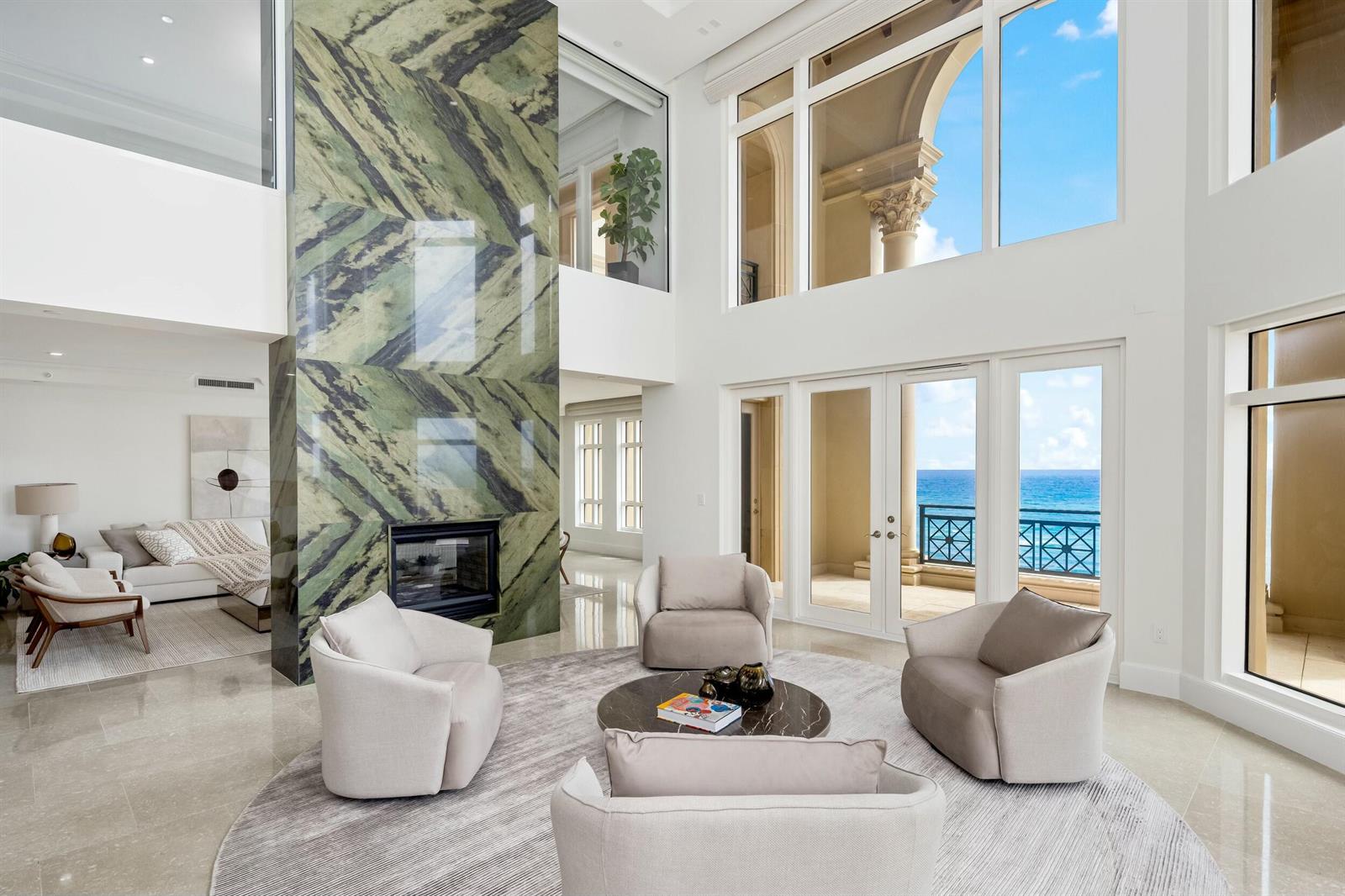 A double-height living room features a green marble fireplace, neutral seating, and ocean views — 2500 S Ocean Boulevard # 903, Boca Raton FL 33432, BOCA RATON, FL