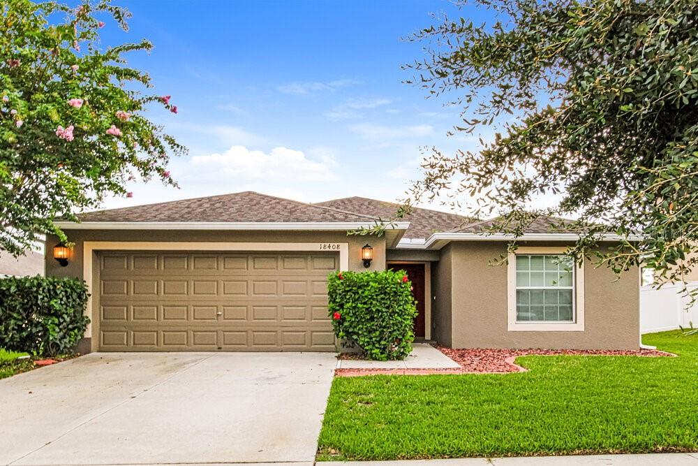A single-story house with a tan stucco exterior, a two-car garage, and a manicured lawn — 18408 WAYDALE LOOP, HUDSON, FL