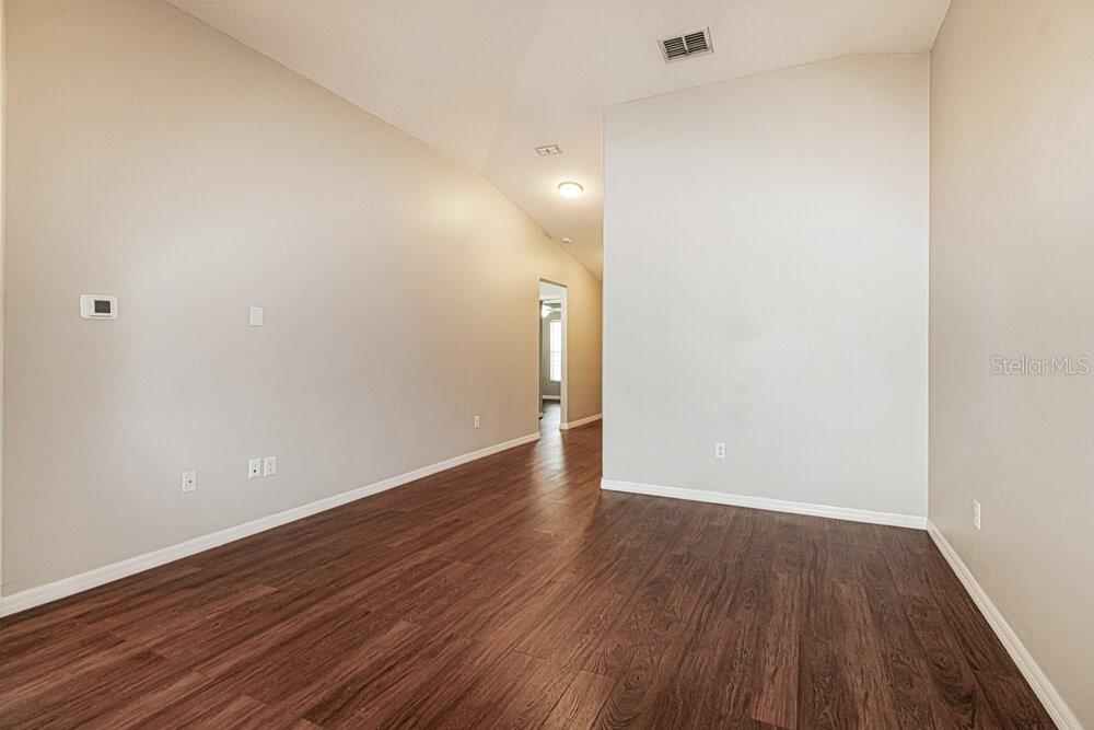 An empty room with vaulted ceilings, light-colored walls, and dark wood-look flooring — 18408 WAYDALE LOOP, HUDSON, FL