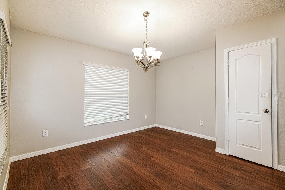 An empty dining room features wood-look flooring, light gray walls, a chandelier, and a white door — 18408 WAYDALE LOOP, HUDSON, FL