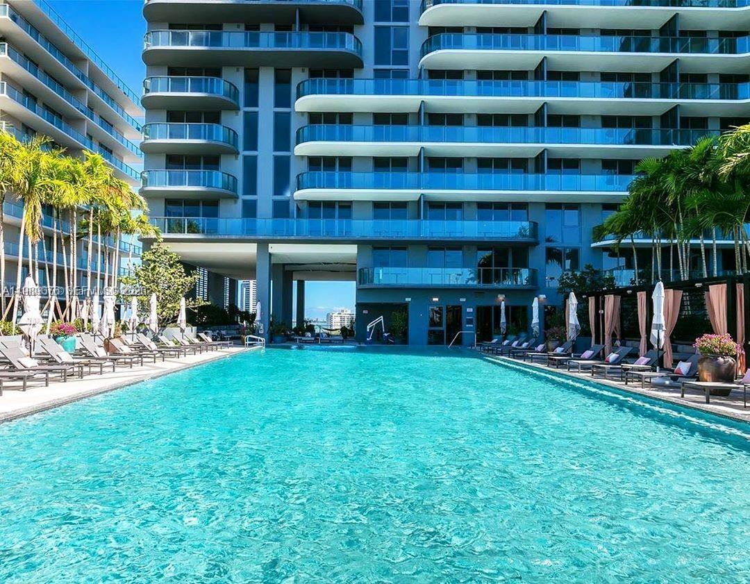 A large swimming pool sits in front of a modern multi-story apartment building — 121 NE 34th St # 2115, Miami FL 33137, MIAMI, FL