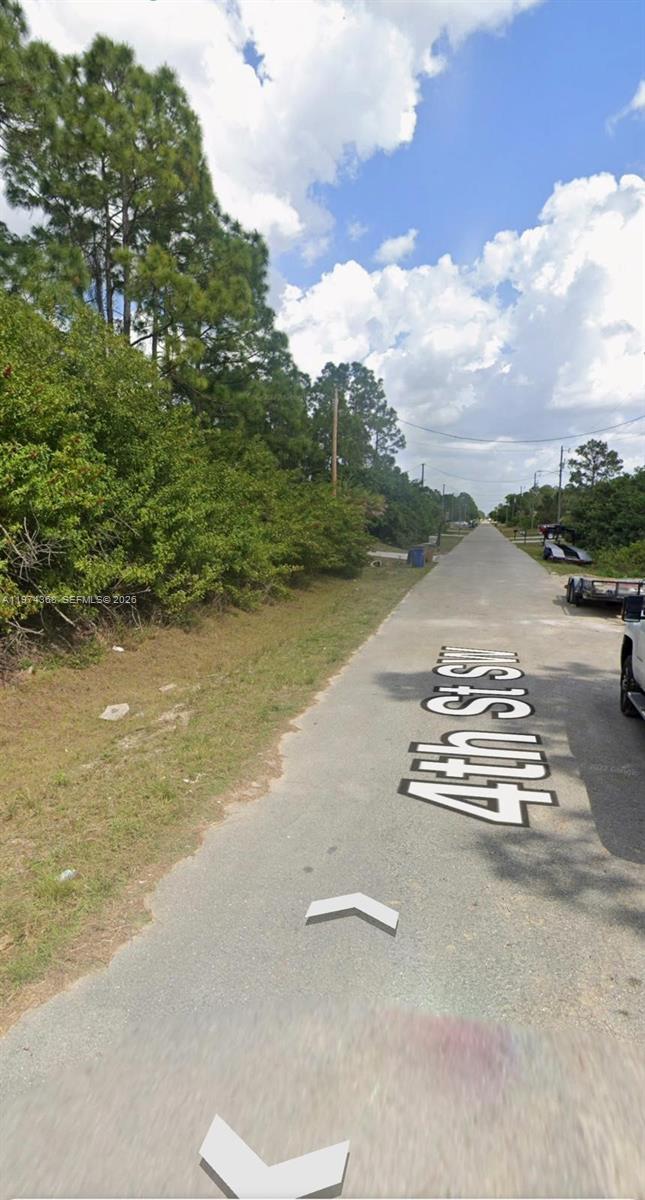 A paved road stretches into the distance, flanked by dense trees and brush — 3620 4TH ST SW, Lehigh Acres FL 33976, LEHIGH ACRES, FL