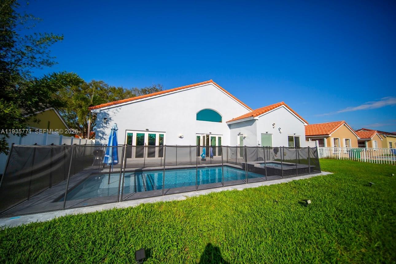 A backyard features a swimming pool with a safety fence and a white house exterior — 13020 SW 17th Ct, Miramar FL 33027, MIRAMAR, FL