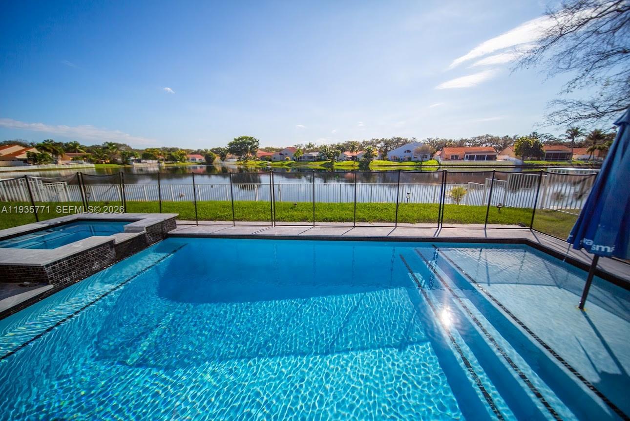 A swimming pool and hot tub overlook a lake behind a residential property — 13020 SW 17th Ct, Miramar FL 33027, MIRAMAR, FL