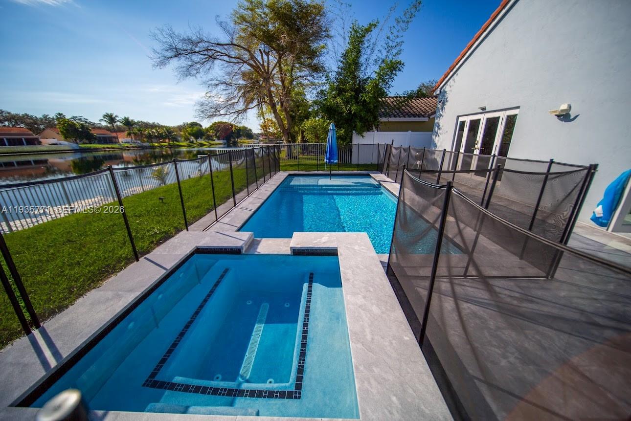 A backyard features a rectangular swimming pool, a hot tub, and a black safety fence — 13020 SW 17th Ct, Miramar FL 33027, MIRAMAR, FL