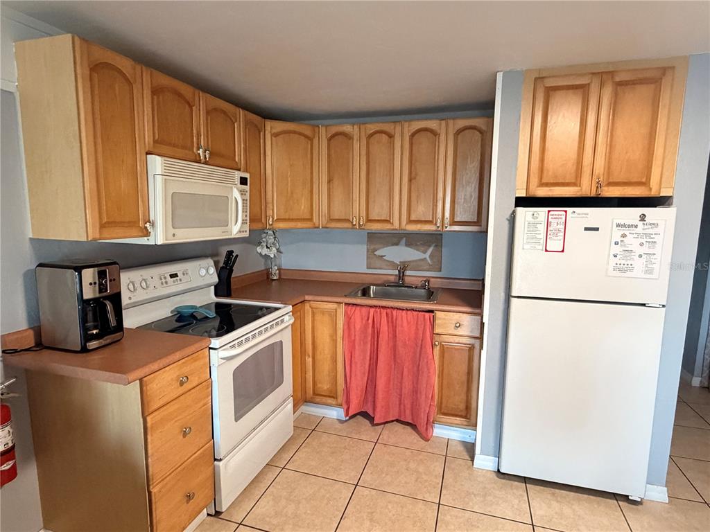 A kitchen features wooden cabinets, a white stove, a microwave, and a white refrigerator — 82 2ND STREET UNIT D5, CEDAR KEY, FL