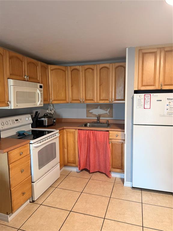 A kitchen features light wood cabinets, white appliances, and a red curtain under the sink — 82 2ND STREET UNIT D5, CEDAR KEY, FL