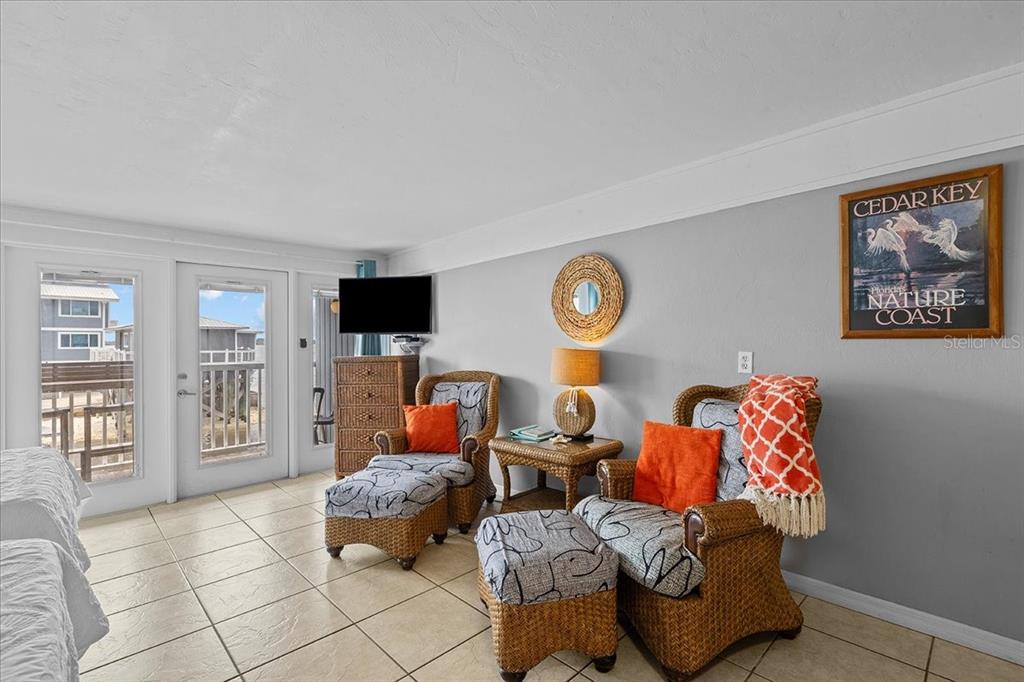 A bedroom features two wicker armchairs with ottomans, a television, and a balcony view — 82 2ND STREET UNIT D5, CEDAR KEY, FL