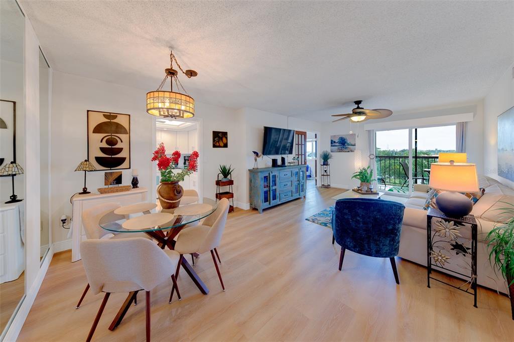 A bright living and dining area features light wood flooring, a glass table, and balcony access — 19029 US HIGHWAY 19 N UNIT 9-403, CLEARWATER, FL