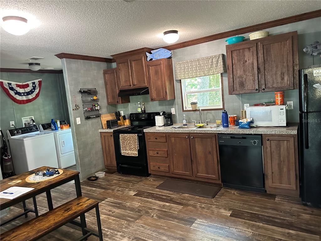 A kitchen with wooden cabinets, black appliances, and a laundry area in the background — 6735 SW 51ST AVENUE, GAINESVILLE, FL