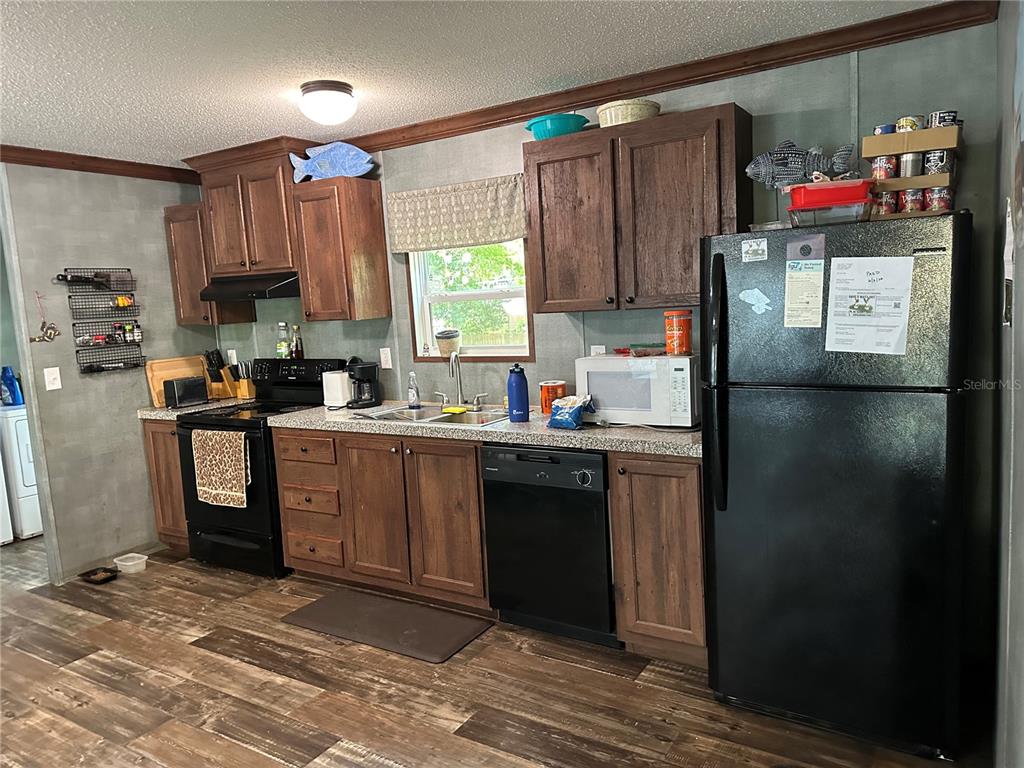 A kitchen features dark wood cabinets, black appliances, and wood-look flooring — 6735 SW 51ST AVENUE, GAINESVILLE, FL
