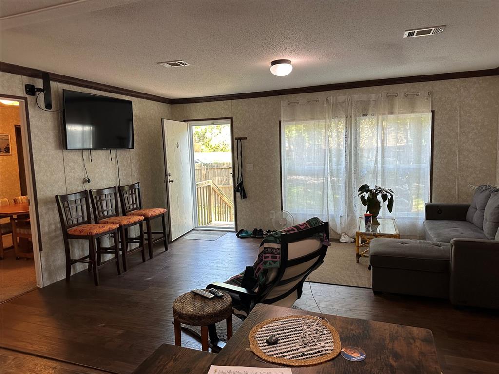 A living room with wood-look flooring, a wall-mounted television, and a sliding glass door — 6735 SW 51ST AVENUE, GAINESVILLE, FL