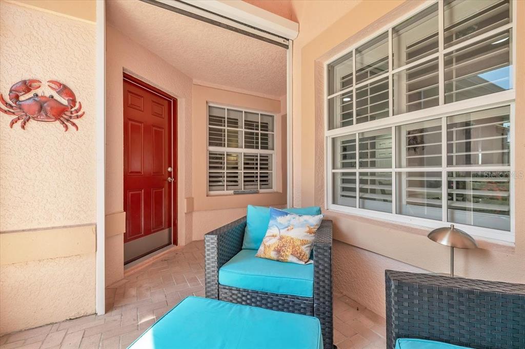 A covered patio features a red door, wicker furniture with blue cushions, and a crab decoration — 1260 RIO DE JANEIRO AVENUE UNIT 102, PUNTA GORDA, FL