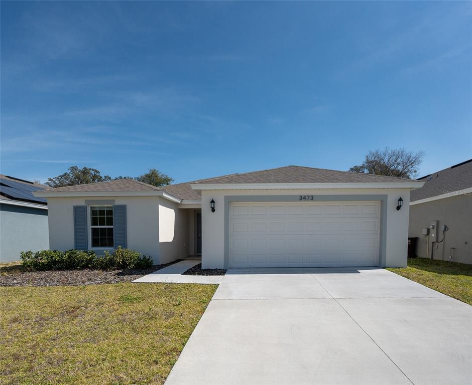 A single-story house with a two-car garage, light-colored stucco walls, and blue shutters — 3473 YARIAN DRIVE, HAINES CITY, FL