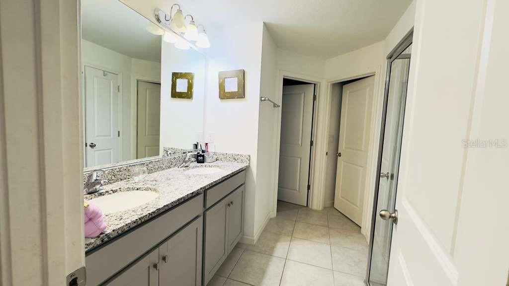 A bathroom features a double vanity with granite countertops, gray cabinets, and a glass shower — 3473 YARIAN DRIVE, HAINES CITY, FL