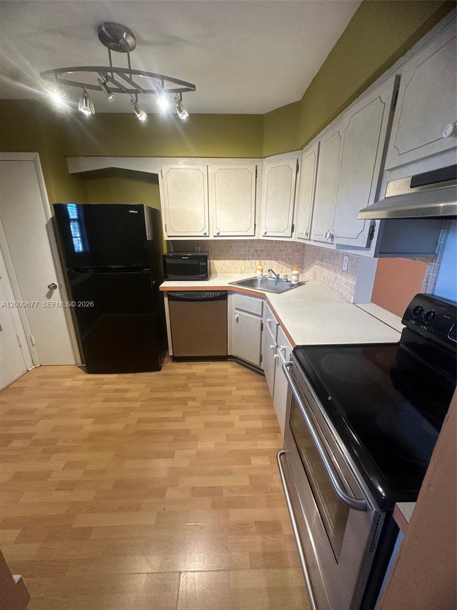 A kitchen features light-colored cabinets, black appliances, a tiled backsplash, and light wood-look flooring — 1530 NE 191st St # 205, Miami FL 33179, MIAMI, FL