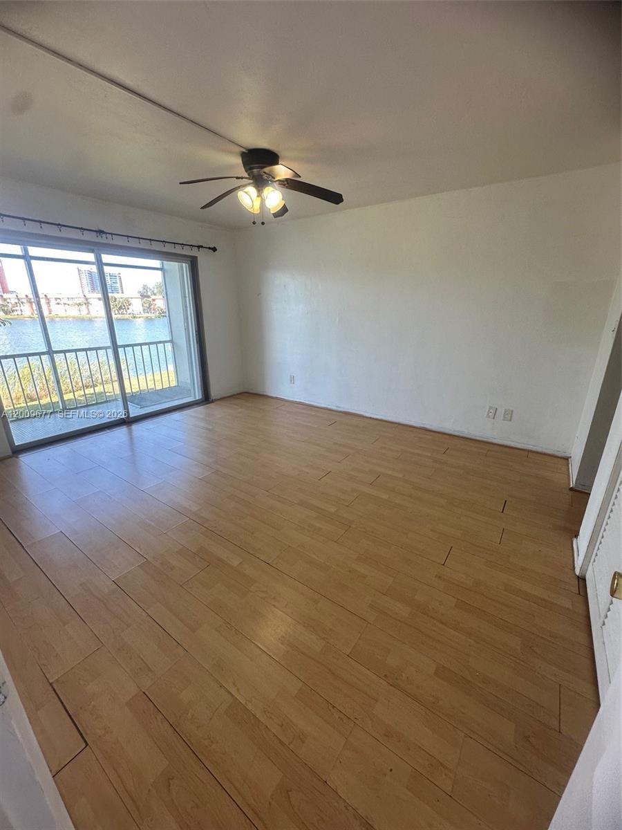 An empty room features light wood-look flooring, a ceiling fan, and a sliding glass door — 1530 NE 191st St # 205, Miami FL 33179, MIAMI, FL